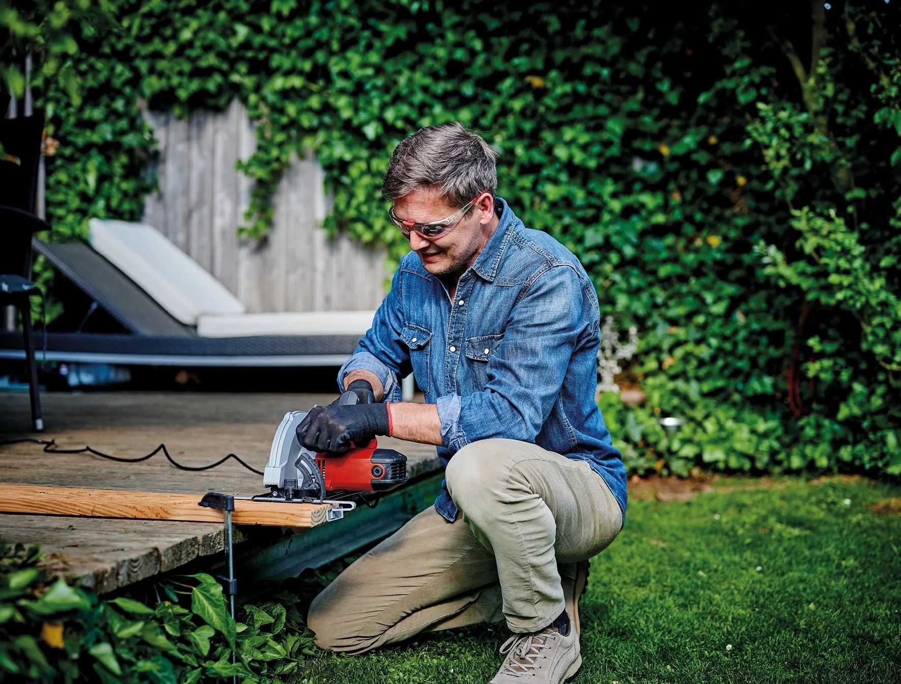Férfi fát vág a piros Einhell TC-CS 1410 kézi körfűrésszel a kertben. Férfi fát vág a piros Einhell TC-CS 1410 kézi körfűrésszel a kertben.