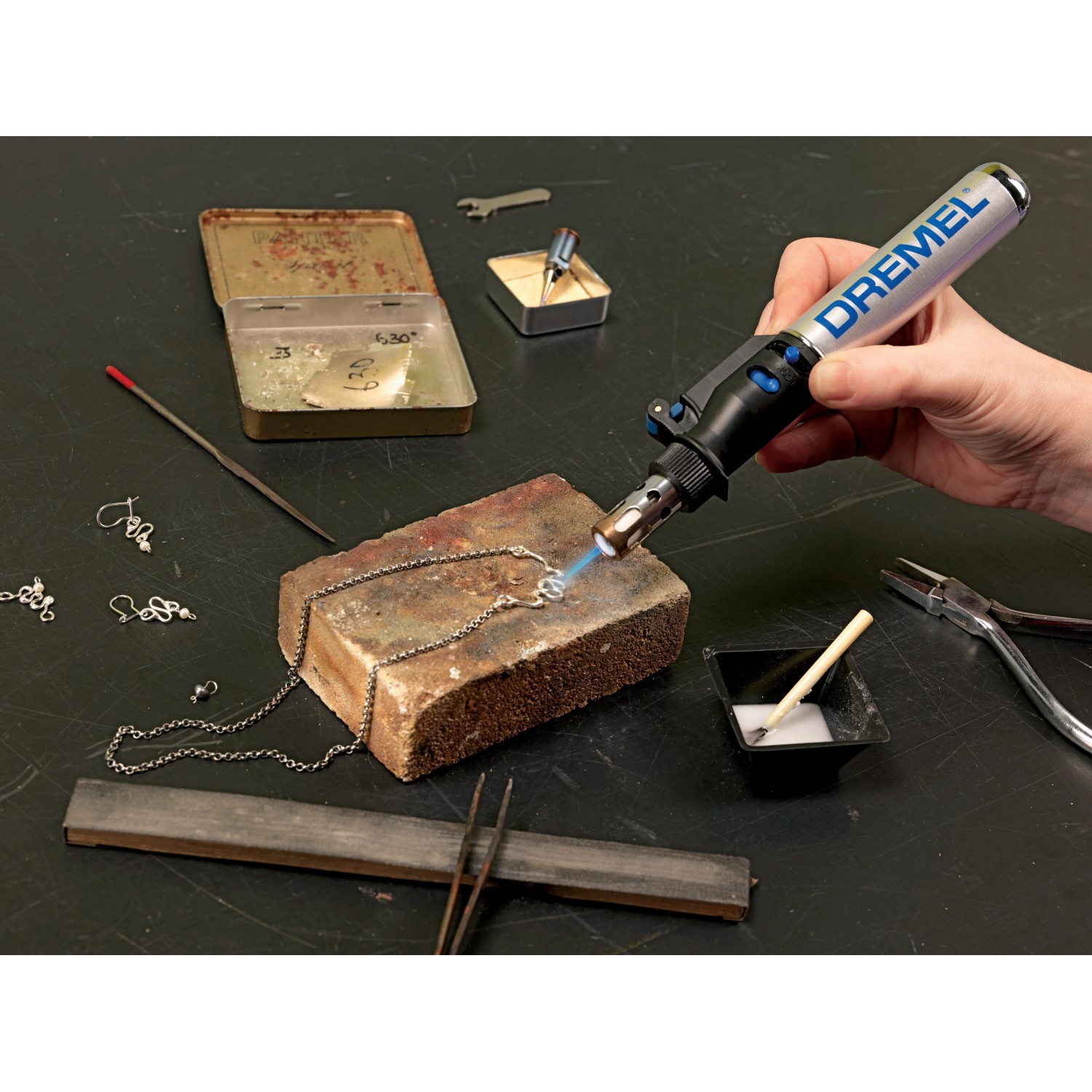 Dremel VersaTip forrasztópáka használat közben ékszerek forrasztásához a munkapadon szerszámokkal. Dremel VersaTip forrasztópáka használat közben ékszerek forrasztásához a munkapadon szerszámokkal.