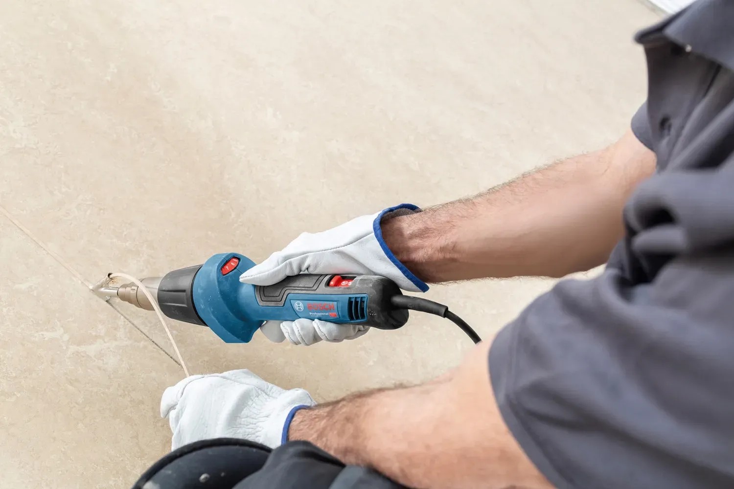Bosch Professional GHG 20-60 hőlégfúvó használat közben, kék, fúvókával és kesztyűvel. Bosch Professional GHG 20-60 hőlégfúvó használat közben, kék, fúvókával és kesztyűvel.