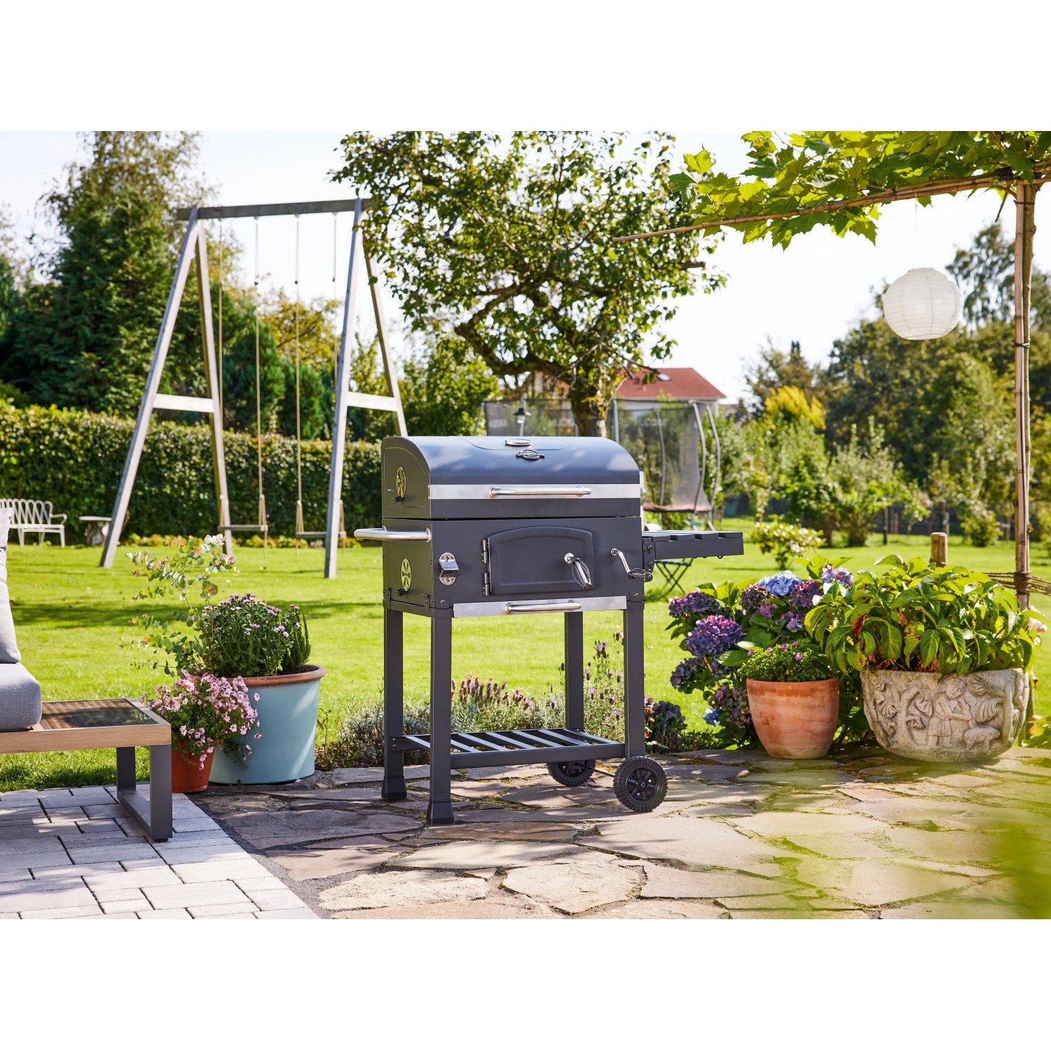 Jamestown Jaxon faszenes grill kocsi oldalsó asztallal és tárolóval a kertben. Jamestown Jaxon faszenes grill kocsi oldalsó asztallal és tárolóval a kertben.
