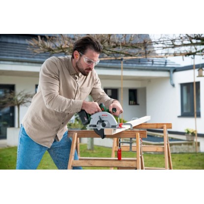 Férfi fát vág Bosch EasyCirc 18V-48 akkus kézi körfűrésszel. Körfűrész működés közben. Férfi fát vág Bosch EasyCirc 18V-48 akkus kézi körfűrésszel. Körfűrész működés közben.
