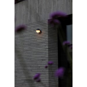 Modern LED kültéri fali lámpa szürke téglafalon. Kerek forma, meleg fény.