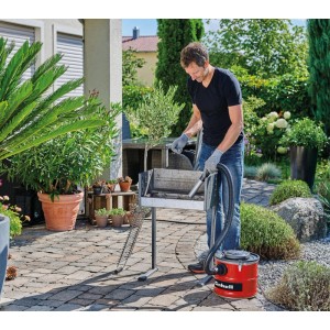 Férfi tisztítja a grillt Einhell TC-AV 1830 D hamuporszívóval. Nedves és száraz porszívó fém szívócsővel.