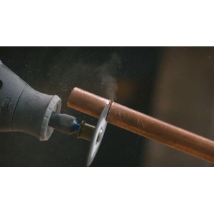 Dremel miniszerszám vág egy rézcsövet vágókoronggal. Por látható a precíz vágás során.