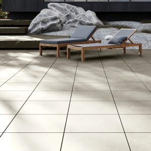 Lerakott bézs Tuscany Stone 60x60 cm-es porcelán kerámia teraszlapok két napozóággyal a kültéri területen.