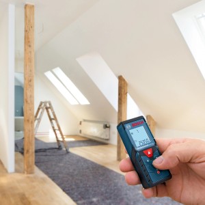 Bosch Professional GLM 40 lézeres távolságmérő a kézben a padlástéri építkezés előtt.