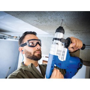 Férfi LUX-TOOLS fekete-átlátszó védőszemüvegben fúr a mennyezetbe. Karcálló, páramentes szemvédelem szíjjal.