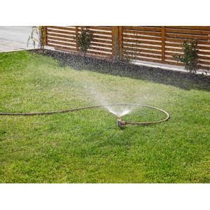 Gardena esőztető öntözi a gyepet. Esőztető tömlővel a zöld területen.