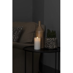 Konstsmide LED valódi viasz gyertya 3D lánggal és olvasztott széllel asztalon, dekoráció mellett.