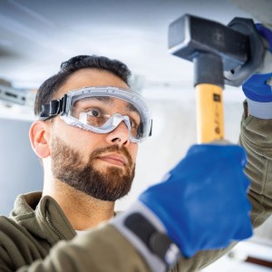 Férfi LUX-TOOLS védőszemüveget visel pánttal kalapálás közben. Szemvédelem barkácsoláshoz.