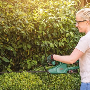 Nő sövényt vág a Bosch EasyHedgeCut 18-45 akkus sövényvágóval. Akkus sövényvágó a pontos vágásokhoz.