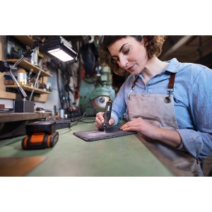 Nő gravíroz egy munkadarabot Worx MakerX akkus multifunkciós szerszámmal. Tartozékokkal.