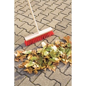 LUX 40 cm-es utcai seprű nyéllel és piros sörtékkel, amint lombot seper a térkövön.