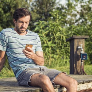 Férfi a Gardena Bluetooth öntözésvezérlőt okostelefonon keresztül működteti a kertben.