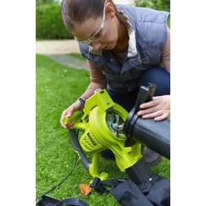 Zöld elektromos lombporszívó/lombfúvó használat közben a gyepen.
