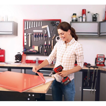 Nő fóliát távolít el Einhell Power X-Change TE-HA 18 Li Solo akkus hőlégfúvóval a műhelyben.