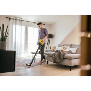 Férfi porszívózza a nappali padlóját egy sárga Kärcher VC 4 Cordless myHome akkus porszívóval.