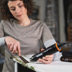 Nő távolít el festéket Worx MakerX 20 V akkus hőlégfúvóval WX743.9. Kompakt hő eszköz kézműves munkákhoz.