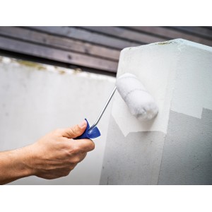 Kéz fest egy betonoszlopot LUX PRO festőhengerrel, szürke.