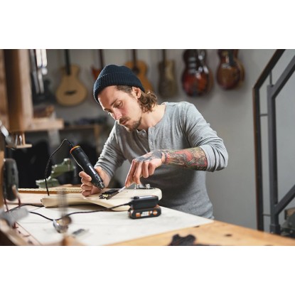 Férfi Worx MakerX 20 V akkus hőlégfúvót használ gitáron. Kompakt hőlégfúvó kézműves munkákhoz.