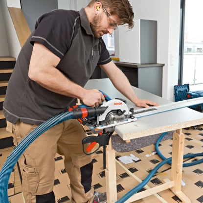 Bosch GKS 18V-57 G akkus körfűrész használat közben porelszívással és vezető sínnel.