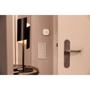 Osram Smart+ WiFi mozgásérzékelő a falra szerelve, lámpa és kilincs mellett.