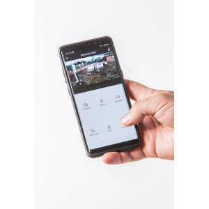Kézben okostelefon a Summer Fun Smart Garden Cam alkalmazással. Kerti kamerás megfigyelés.