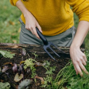 Nő Fiskars Solid ültetővillát használ a talaj megmunkálásához a kerti ágyásban.