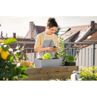 Nő Lechuza Balconera Stone 50 virágládával, kőszürke színben, növényekkel a balkonon.