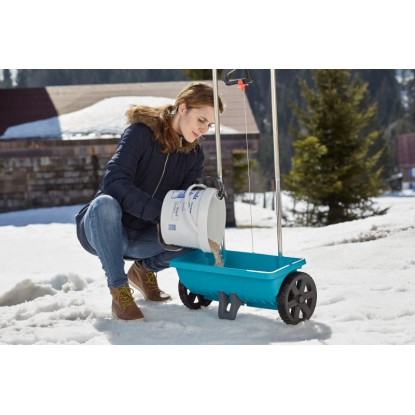 Nő tölti fel a Gardena L szórókocsit műtrágyával vagy sóval télen.
